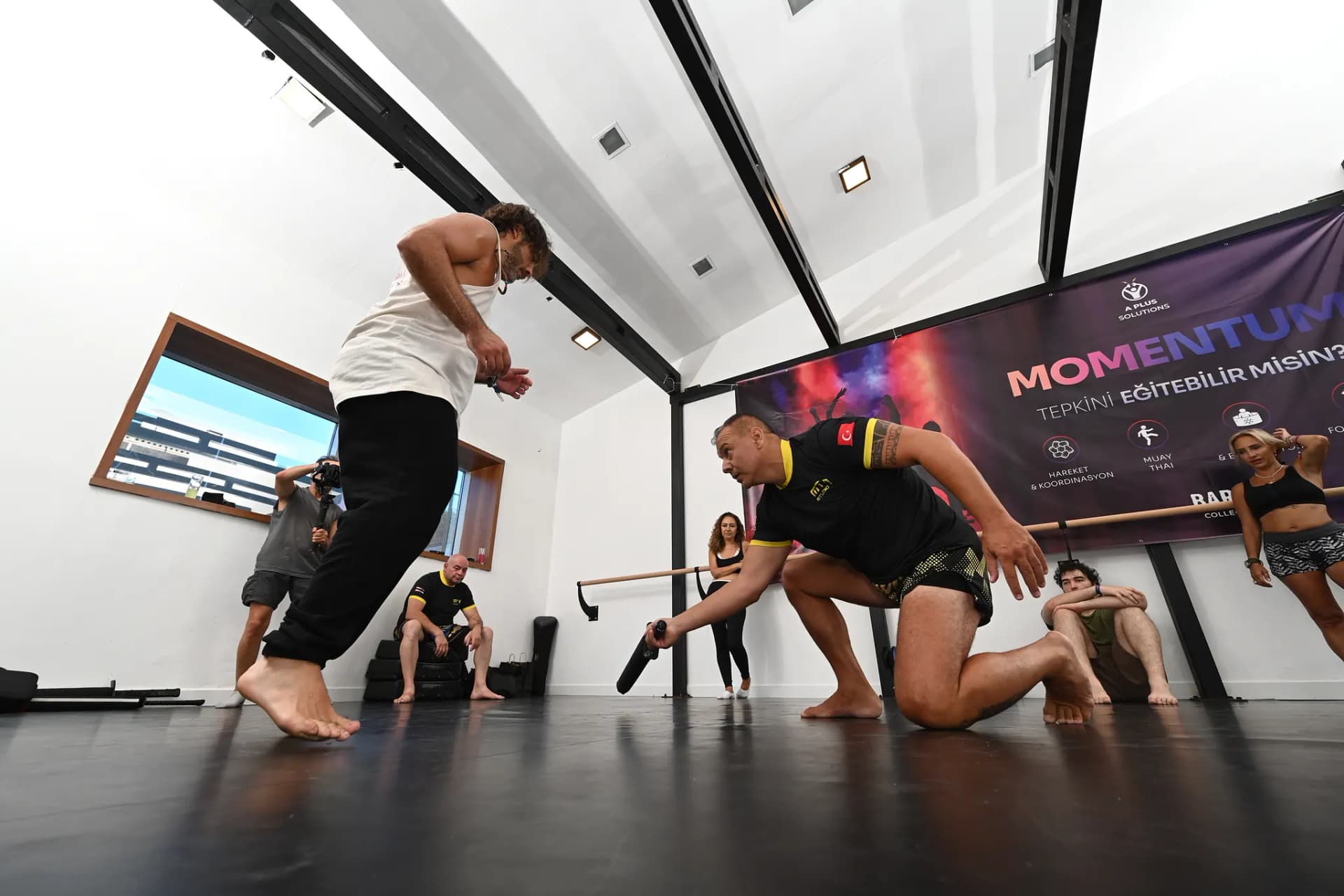 Çömelip sopayla refleks çalıştıran muay thai koçu